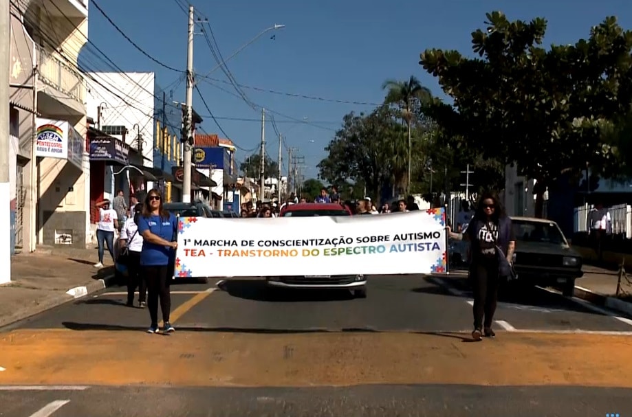 Imagem da caminhada acontecendo, onde duas pessoas seguram uma faixa.