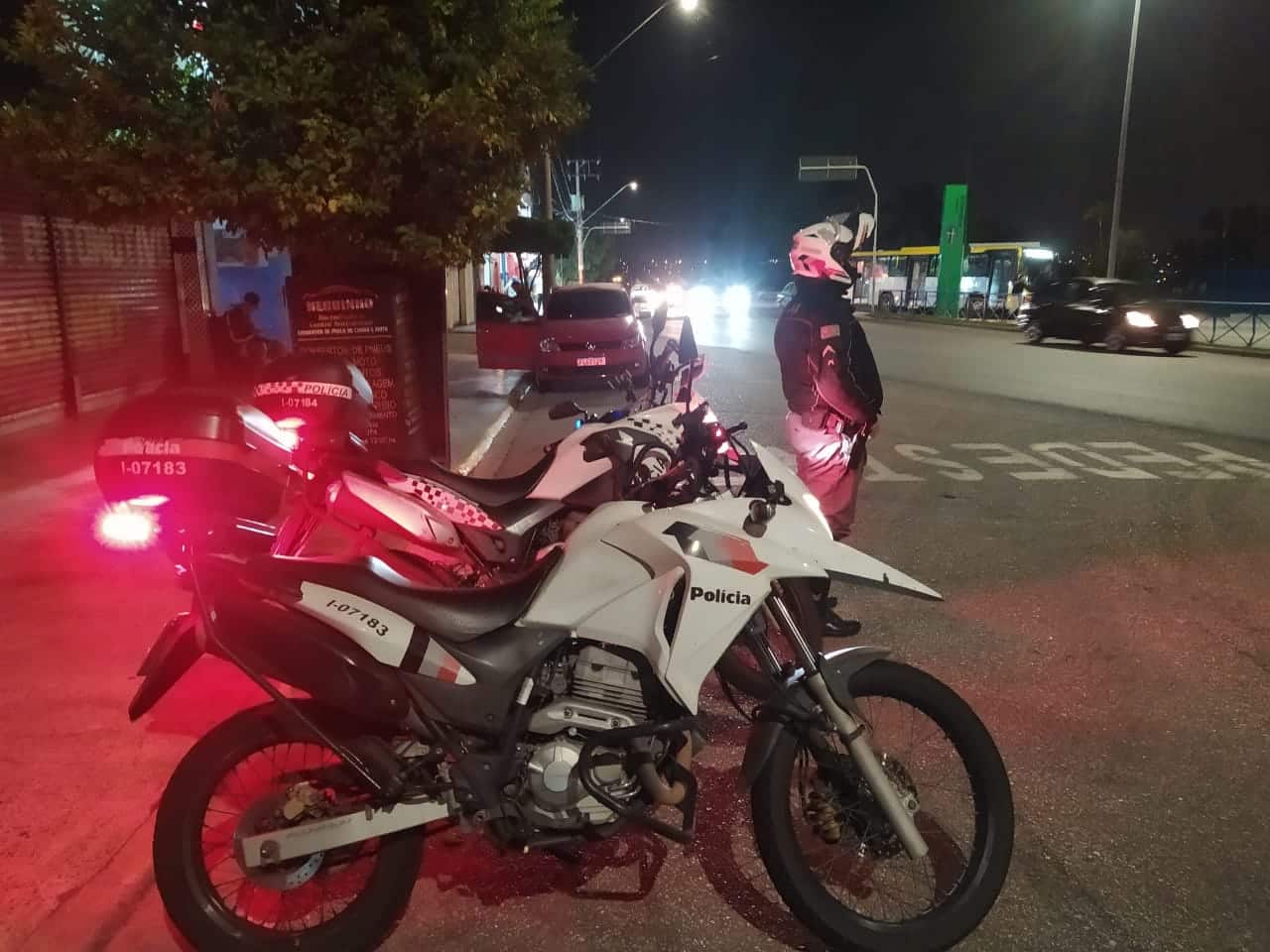 Imagem de policial ao lado de duas motos na rua.