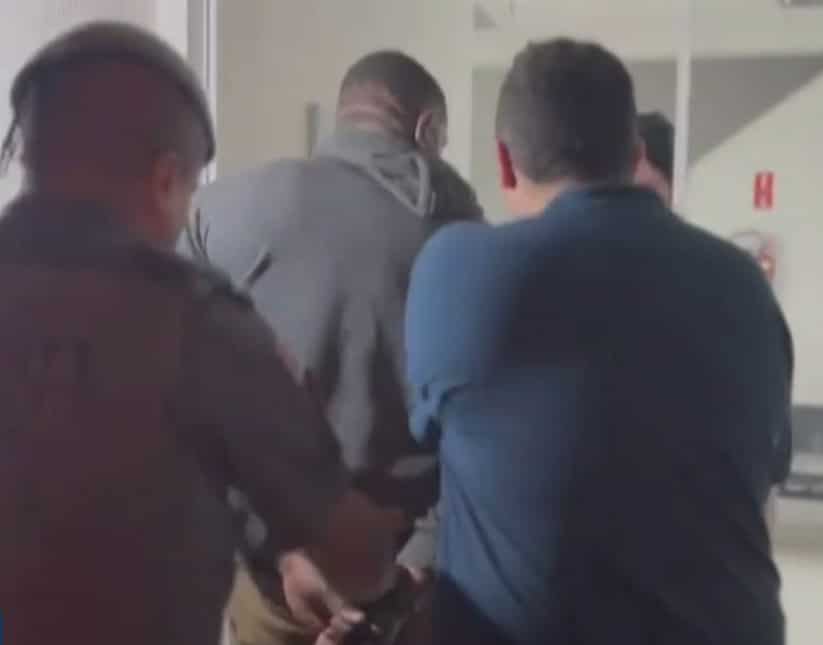 Imagem de suspeito sendo levado pela polícia até a delegacia.