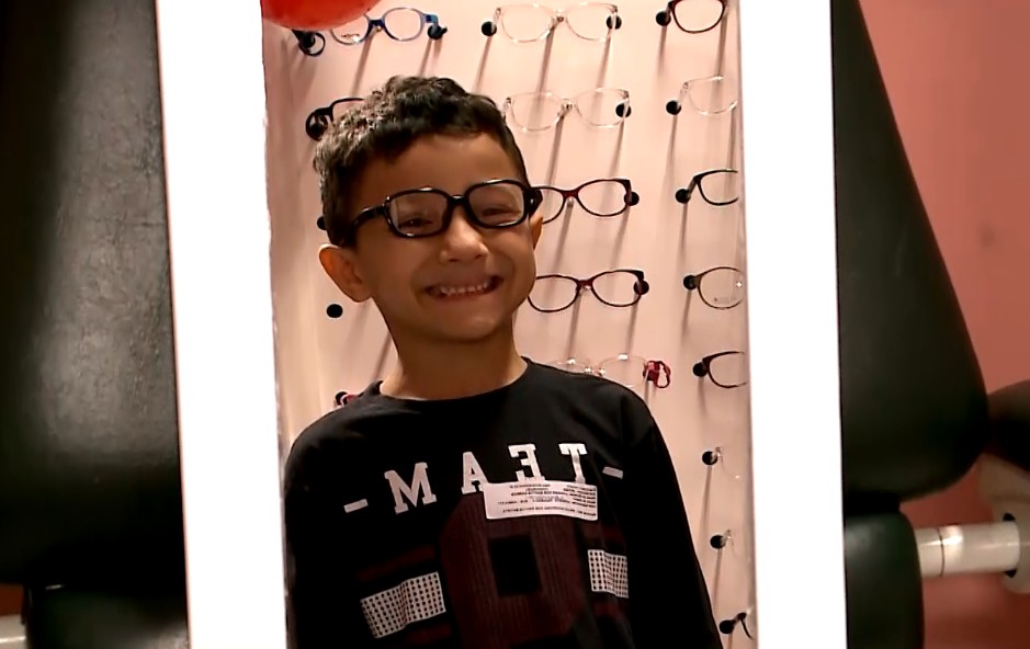 Menino usando &oacute;culos em frente a um espelho.